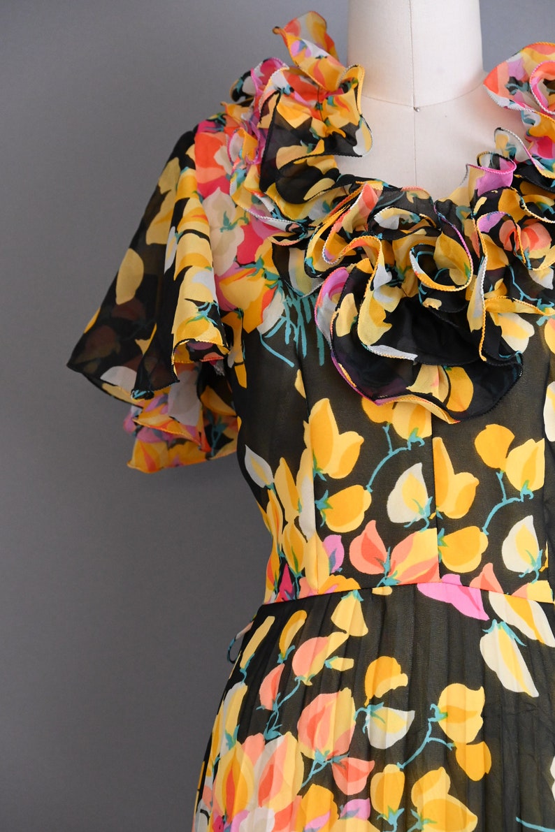 May include: A black sheer dress with a floral print in yellow, pink, and white. The dress has a ruffled neckline and short sleeves.