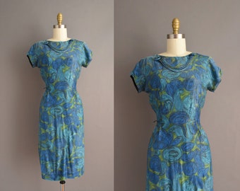 May include: A blue and green vintage dress with a floral print. The dress has a scoop neck and short sleeves. It is fitted through the bodice and flares out slightly at the skirt.