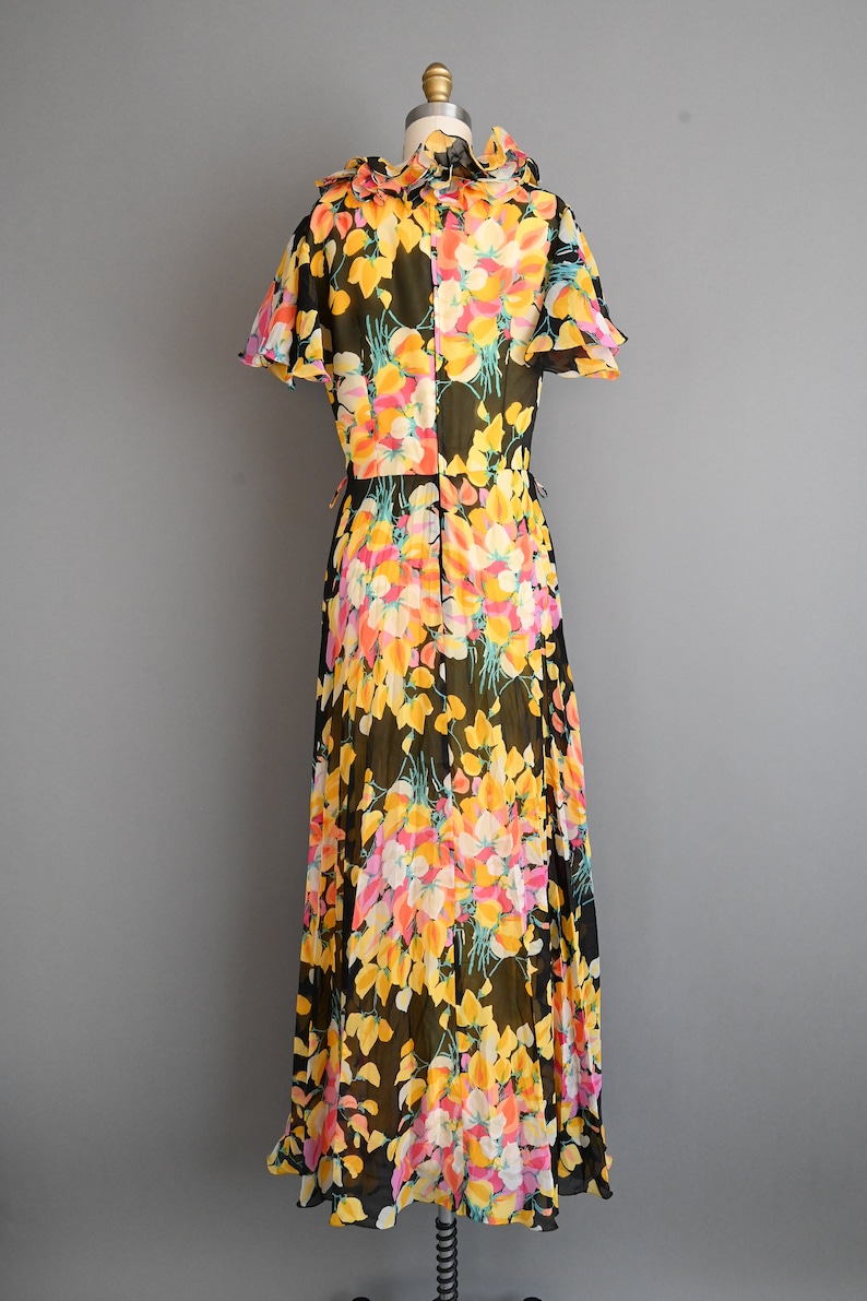 May include: A long black maxi dress with a floral print in shades of yellow, pink, and white. The dress has a ruffled neckline and short sleeves.