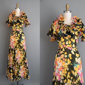 May include: A black and yellow floral print maxi dress with a large ruffled collar. The dress is made of sheer fabric and has a pleated skirt.