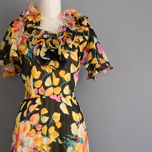 May include: A black and yellow floral print dress with a ruffled neckline and short sleeves. The dress is made of a sheer fabric and has a pleated skirt.