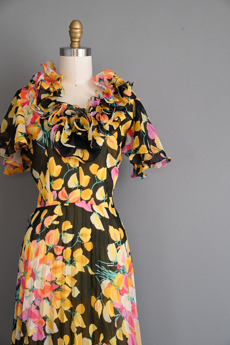 May include: A black and yellow floral print dress with a ruffled neckline and short sleeves. The dress is made of a sheer fabric and has a pleated skirt.