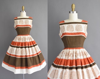 May include: A sleeveless vintage dress with a brown, orange, and white striped pattern. The dress has a fitted bodice and a full skirt.