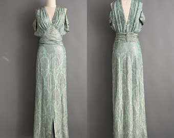 Könnte beinhalten: Ein bodenlanges Vintage-Kleid aus hellgrünem und silbernem floralem Brokat. Das Kleid hat einen V-Ausschnitt, drapierte Ärmel und eine schmale Taille. Der Rücken hat einen V-Ausschnitt und einen Knopfverschluss. Der Rock hat einen Schlitz vorne.