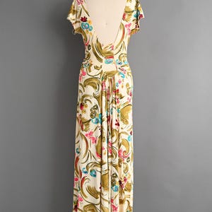 May include: A vintage-style, floor-length dress on a mannequin. The dress features a cream-colored background with a floral pattern in pink, blue, and gold. It has short sleeves and a low back.