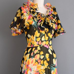 May include: A black and yellow floral print dress with a ruffled neckline and short sleeves. The dress is made of a sheer fabric and has a pleated skirt.