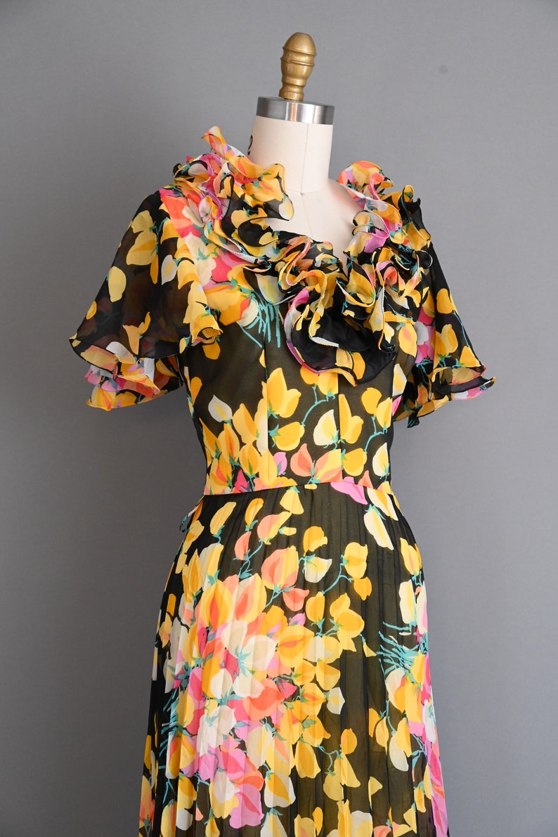 May include: A black and yellow floral print dress with a ruffled neckline and short sleeves. The dress is made of a sheer fabric and has a pleated skirt.