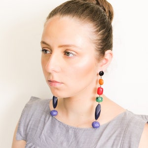 May include: Long, colorful earrings with a variety of shapes and colors, including black, orange, red, green, and blue. The earrings are made of beads and have a dangling design. The earrings are a statement piece.
