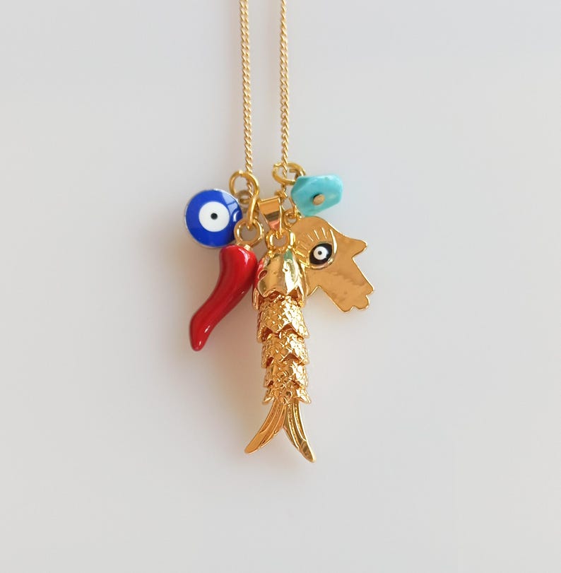Puede incluir: Collar de cadena dorada con m&uacute;ltiples dijes, incluyendo un chile rojo, un ojo turco azul, una flor turquesa y un dije de pez dorado. Los dijes est&aacute;n unidos a una cadena dorada.