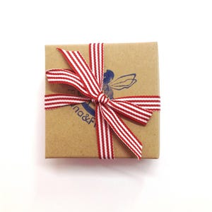 May include: A small brown box with a red and white striped ribbon tied in a bow. The box has a blue stamp with a fairy design and the text "na&F".