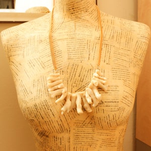 May include: A white coral necklace with a gold chain. The necklace is displayed on a mannequin with a patterned background.