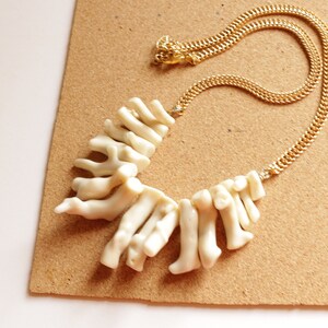 May include: A white coral necklace with a gold chain. The coral is arranged in a fan shape and is attached to the chain with a gold clasp.