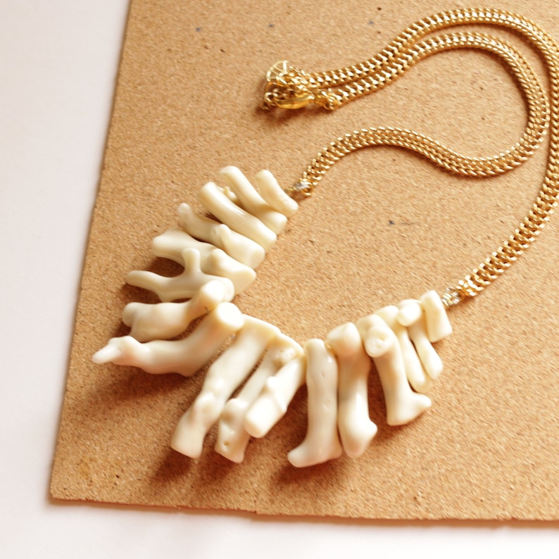 May include: A white coral necklace with a gold chain. The coral is arranged in a fan shape and is attached to the chain with a gold clasp.