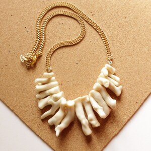 May include: A white coral necklace with a gold chain. The coral is arranged in a fan shape and hangs from the chain.