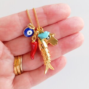 Puede incluir: Collar de cadena dorada con m&uacute;ltiples encantos, incluyendo un ojo turco azul, un chile rojo, un encanto azul turquesa y un encanto de pez dorado.