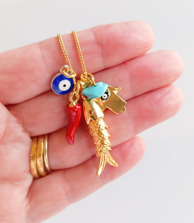 Puede incluir: Collar de cadena dorada con m&uacute;ltiples encantos, incluyendo un ojo turco azul, un chile rojo, un encanto azul turquesa y un encanto de pez dorado.
