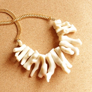 May include: A white coral necklace with a gold chain. The coral pieces are arranged in a cascading pattern.