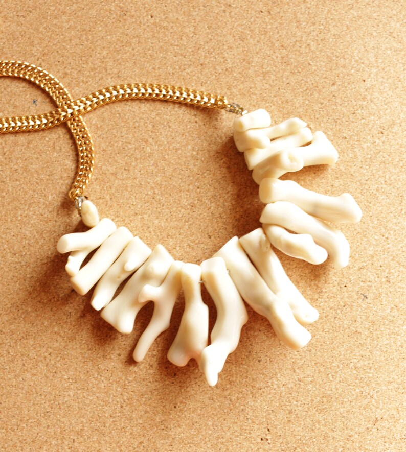 May include: A white coral necklace with a gold chain. The coral pieces are arranged in a cascading pattern.