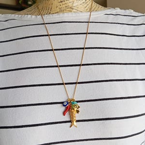 Puede incluir: Un collar de cadena dorada con un dije de un pez dorado, un chile rojo y un dije de ojo turco azul.
