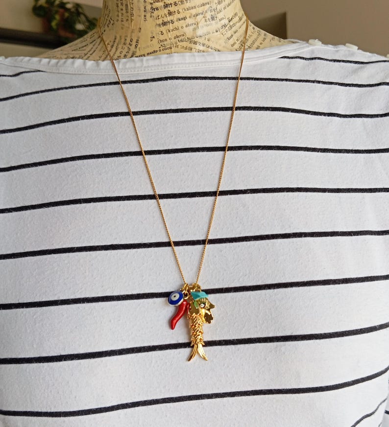 Puede incluir: Un collar de cadena dorada con un dije de un pez dorado, un chile rojo y un dije de ojo turco azul.