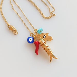 Puede incluir: Collar de cadena dorada con m&uacute;ltiples dijes, incluyendo un chile rojo, un ojo turco azul, una cuenta turquesa y un dije de pez dorado.