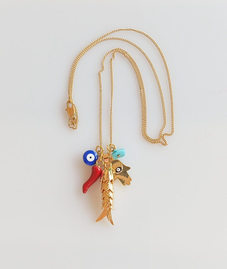 Puede incluir: Collar de cadena dorada con un dije de pez dorado, un chile rojo, un dije de ojo turco azul y una mano turquesa con un dije de ojo turco.