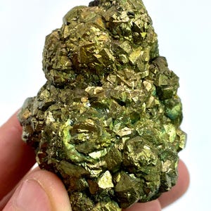 Puede incluir: Un racimo de mineral de pirita en bruto con numerosos cristales cúbicos metálicos de color amarillo latón. El espécimen muestra una superficie compleja y multifacética con formas geométricas doradas reflectantes sobre su forma irregular y texturizada.