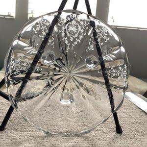 May include: A clear glass pedestal cake plate with a scalloped edge and etched floral design. The plate has three feet.