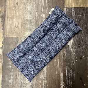 May include: A blue and white patterned fabric microwave heat pack. The pack is rectangular and has three sections.