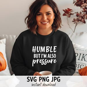 以下が含まれることがあります： 「HUMBLE BUT I'M ALSO pressure」の白文字がプリントされた黒いスウェットシャツ。画像には「SVG PNG JPG instant download」の文字も含まれています。画像内の人物は白いマグカップを持っています。