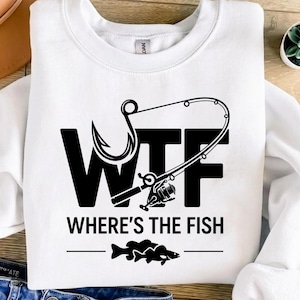 May include: White crew neck sweatshirt featuring a black graphic. The graphic reads "WTF WHERE'S THE FISH" with a fishing hook and rod design. Below the text is a graphic of two fish. The sweatshirt is a casual style.