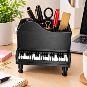 Può includere: Un organizer da scrivania a forma di pianoforte nero con una tastiera dai tasti bianchi e neri. Lo scomparto superiore contiene vari articoli da ufficio, tra cui due penne nere, un paio di forbici nere, una clip dorata, una penna rossa e un righello.