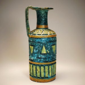 May include: A decorative ceramic vase with a handle, featuring a teal and gold color scheme. The vase has geometric patterns in yellow and teal, with a textured surface. The vase is approximately 12 inches tall.