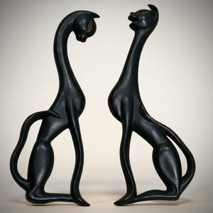 May include: Two black cat sculptures with elongated necks and bodies. The cats are in a seated position, with one looking down and the other looking up. Each cat has red accents on the eyes. The sculptures have a smooth, matte finish.
