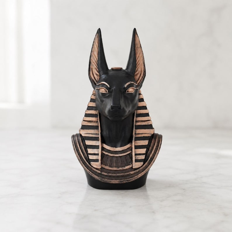 May include: A black Anubis bust with gold accents. The statue features the jackal-headed deity with tall, pointed ears and a detailed collar. The bust is a decorative item, likely for home decor or display.