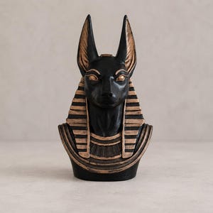 May include: A black Anubis bust with gold accents. The statue features the jackal-headed god of the afterlife, with detailed facial features and a striped headdress. The bust is a decorative item, likely for home decor or display.