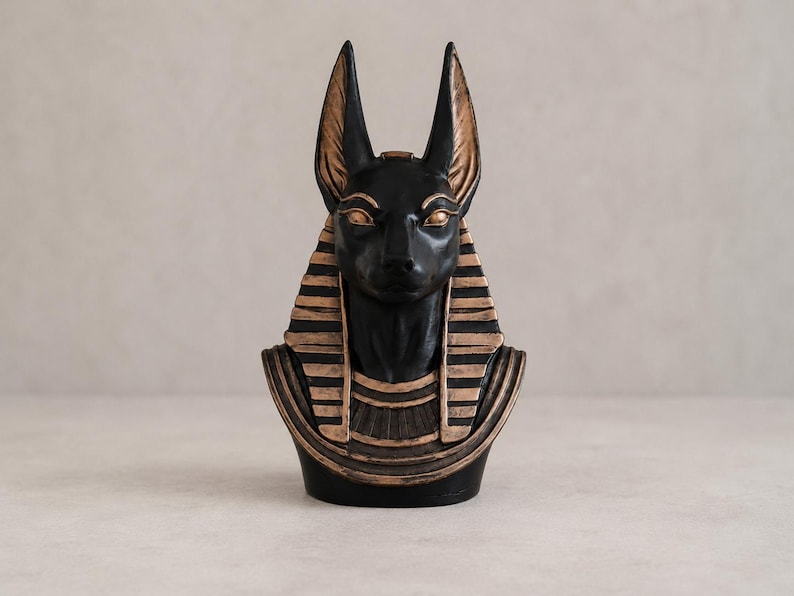 May include: A black Anubis bust with gold accents. The statue features the jackal-headed god of the afterlife, with detailed facial features and a striped headdress. The bust is a decorative item, likely for home decor or display.
