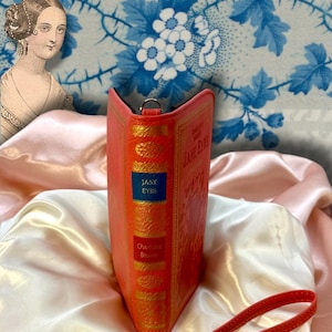 Spine detail of Jane Eyre wallet standing upright on ivory satin fabric, resembling a classic novel spine