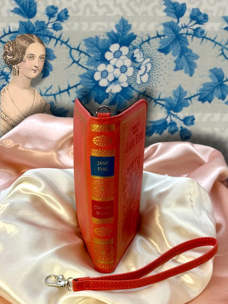Spine detail of Jane Eyre wallet standing upright on ivory satin fabric, resembling a classic novel spine