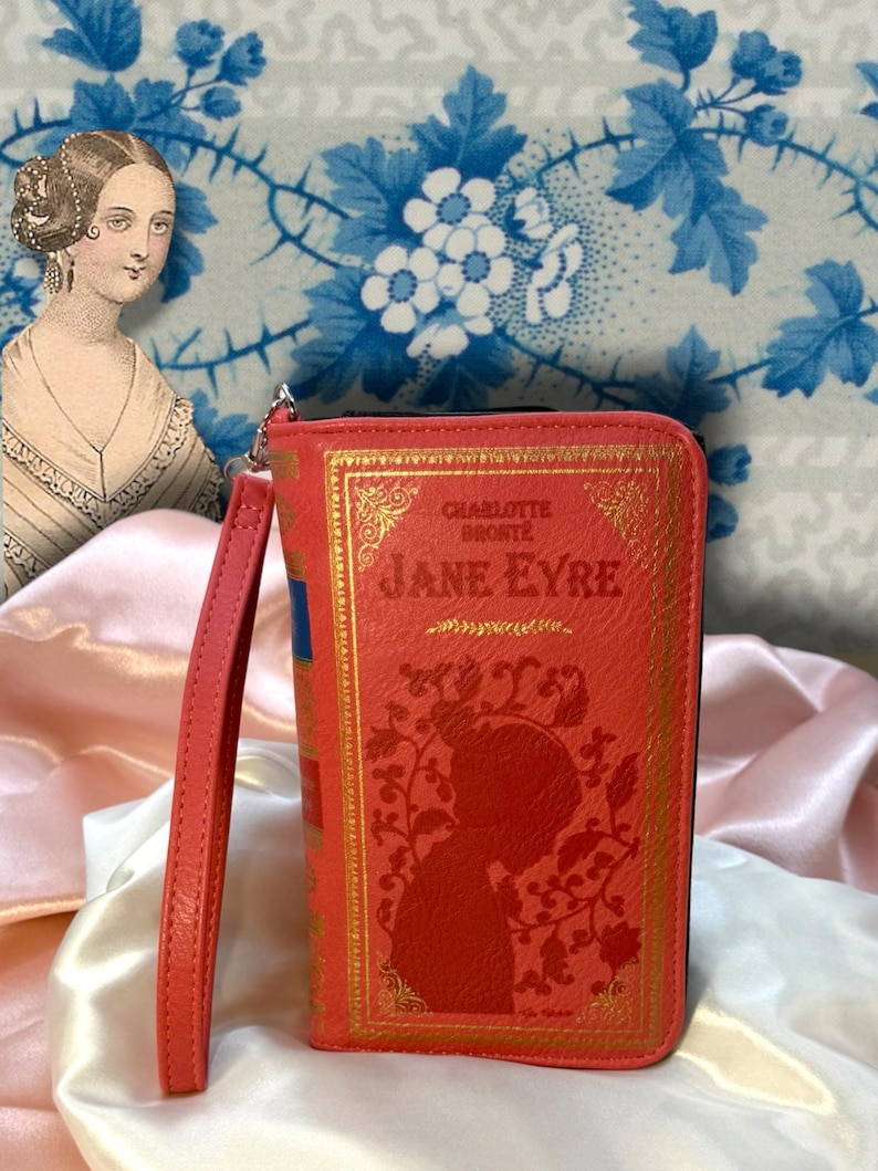 Jane Eyre book wallet standing upright on ivory satin fabric with soft folds, showing classic literary cover and attached wristlet strap
