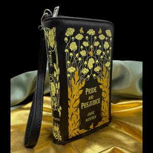 May include: Black clutch with a gold floral design and the title "Pride and Prejudice" by Jane Austen. The clutch has a wrist strap and a zipper closure. The design is reminiscent of a classic book cover.
