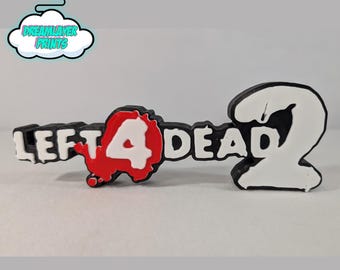 Może przedstawiać: Czarno-białe logo "Left 4 Dead 2" wydrukowane w 3D. Cyfra "4" jest biała z czerwonym wzorem rozprysku. Cyfra "2" jest biała z czarnym obrysem. Tekst "LEFT 4 DEAD" jest biały.