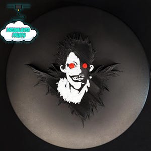 May include: A black and white 3D-printed character with red eyes, wings, and spiky hair. The character is set against a black circular background. The text "DREAMLAYER PRINTS" is in a cloud-shaped logo in the upper left corner.