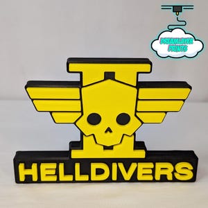 May include: A 3D-printed HellDivers logo in black and yellow. The design features a skull with wings and the word "HELLDIVERS" at the base. The logo is a solid, three-dimensional object.
