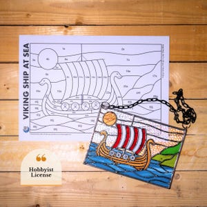 Peut inclure: Un vitrail représentant un navire viking en mer, avec des voiles rayées rouges et blanches, une coque orange et de l'eau bleue. L'image comprend un guide de coloriage avec le texte "VIKING SHIP AT SEA".