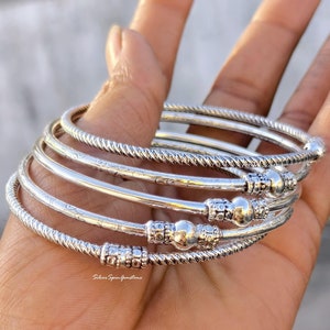 May include: A set of five silver bangles with a textured design and a small ball accent on each bangle.