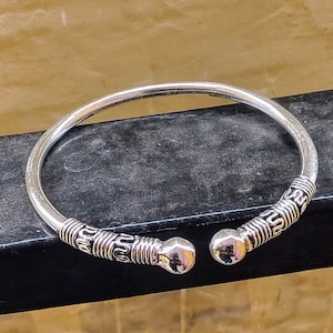 May include: A silver bangle bracelet with a textured design and rounded ends.