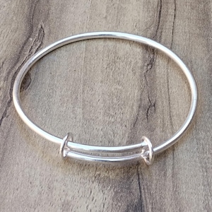 Könnte beinhalten: Ein silbernes, verstellbares Armkettchen mit schlichtem Design. Das Armband besteht aus einem dünnen, runden Draht und hat einen federbelasteten Verschluss.