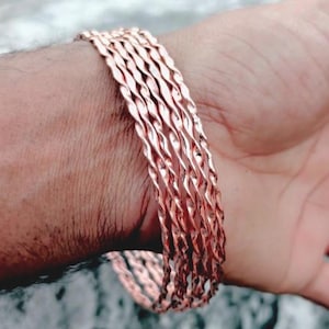 May include: A set of copper-colored bangles with a twisted rope design. The bracelets are stacked on a wrist, showcasing their intricate pattern and warm metallic hue. The bangles are a simple yet elegant accessory.