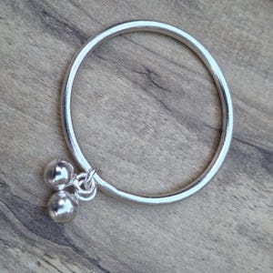 May include: A silver bangle bracelet with two small silver bells hanging from it.